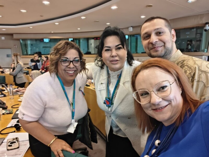 Three women and a man look at the camera in the European Parliament chamber.