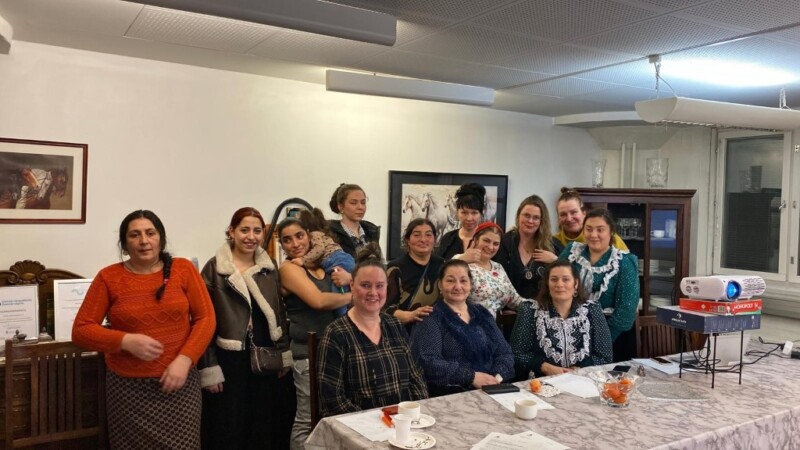 Joukko naisia poseeraa kameralle, osa pöydän ääressä istuen, osa seisten.