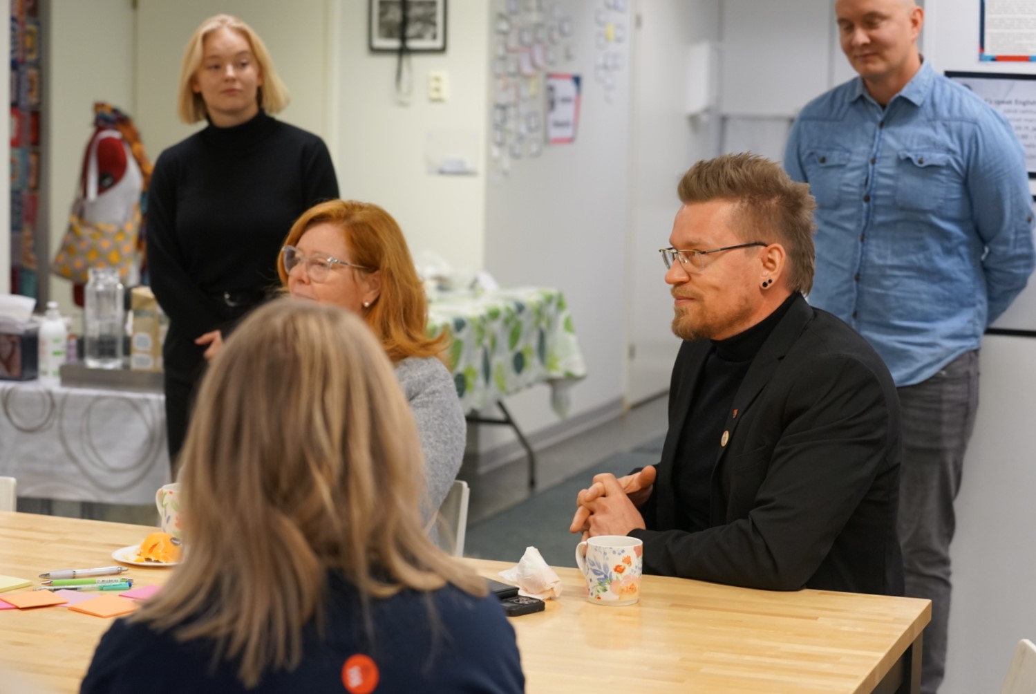 Ryhmä ihmisiä kokoontuneena pöydän äärelle seuraamaan esitystä.