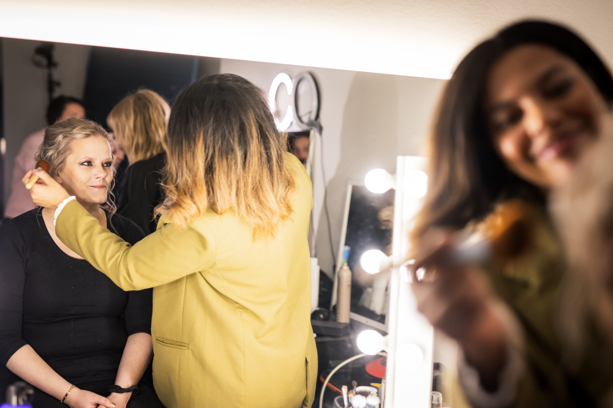 Nainen istuu meikattavana.