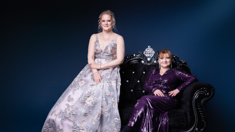 Kaksi naista istuu rinnakkain koristeellisella sohvalla.