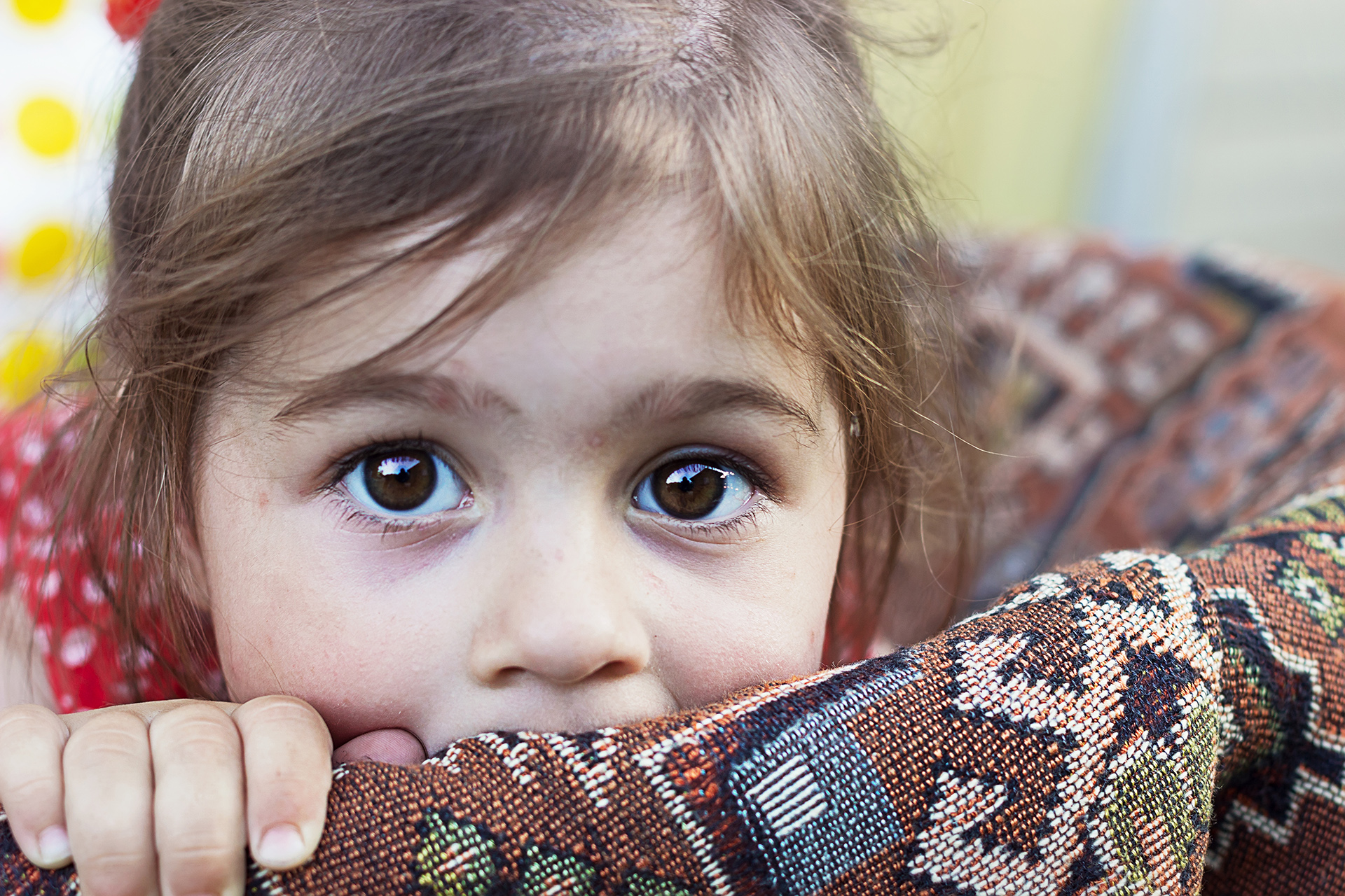 Lähikuva huolestuneen näköisestä pikkutytöstä, joka nojaa kirjokuvioituun tyynyyn.