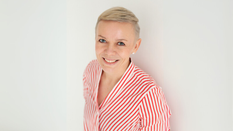 Raitapaitainen nainen hymyilee.