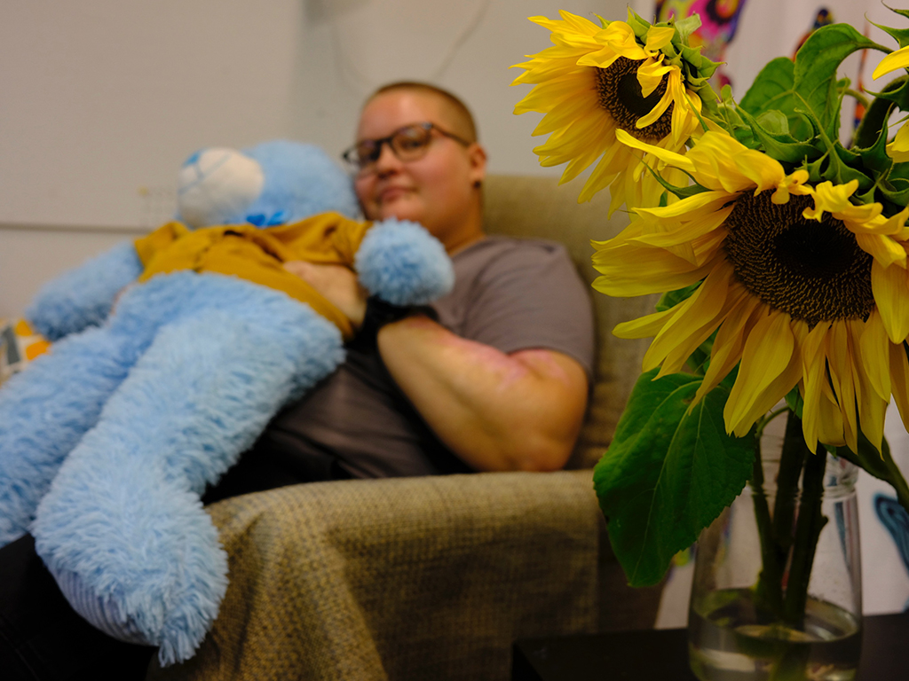 Nuori aikuinen istuu tuolilla ja pitää vaaleansinistä nallea sylissään.