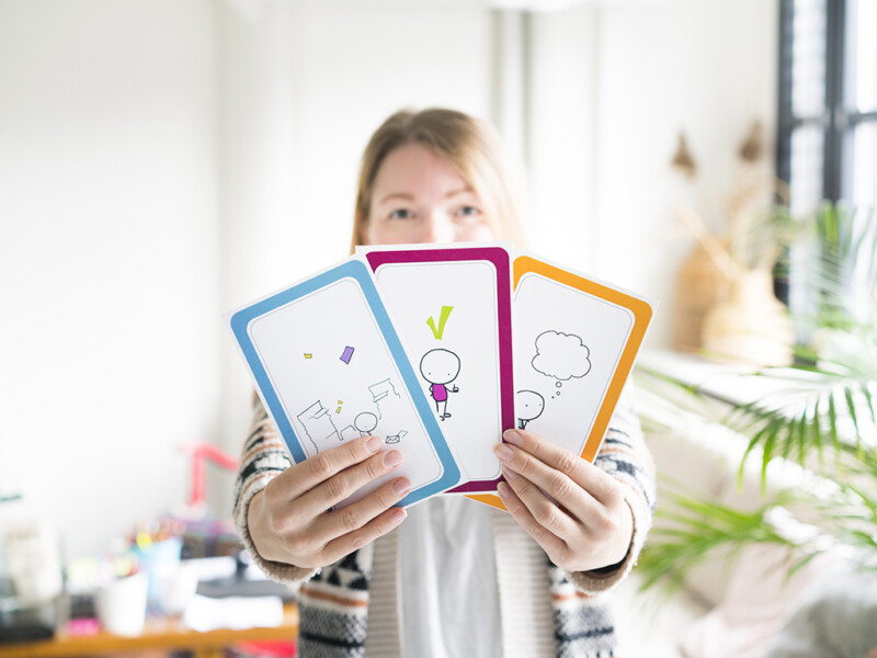 Nainen pitää kädessään kolmea kuvakorttia, jotka osoittavat suoraan kameraan.