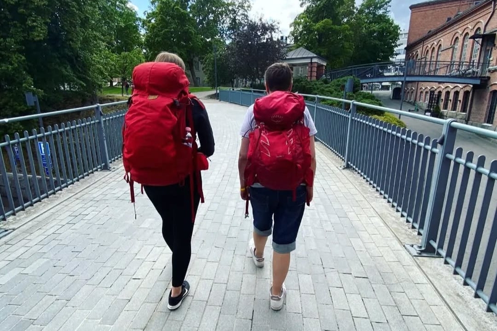 Kaksi kadulla punaiset reput selässä kulkevaa henkilöä kuvattuna takaapäin.