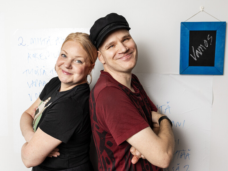 Nainen ja mies nojaavat selkä selkää vasten ja hymyilevät.