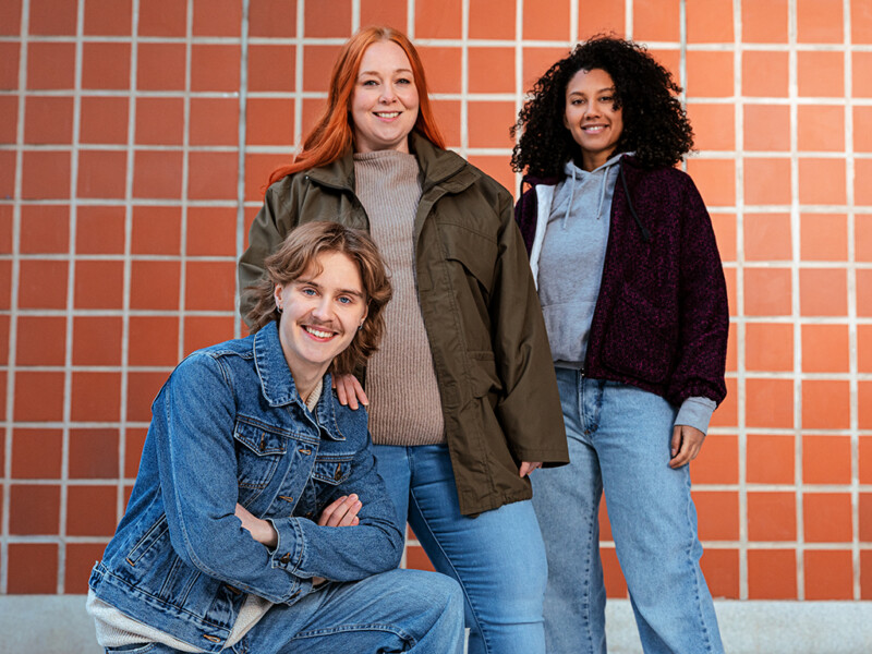 Yritysvapaaehtoisuus - kolme nuorta aikuista seisoo punaisen tiiliseinän edessä hymyillen.