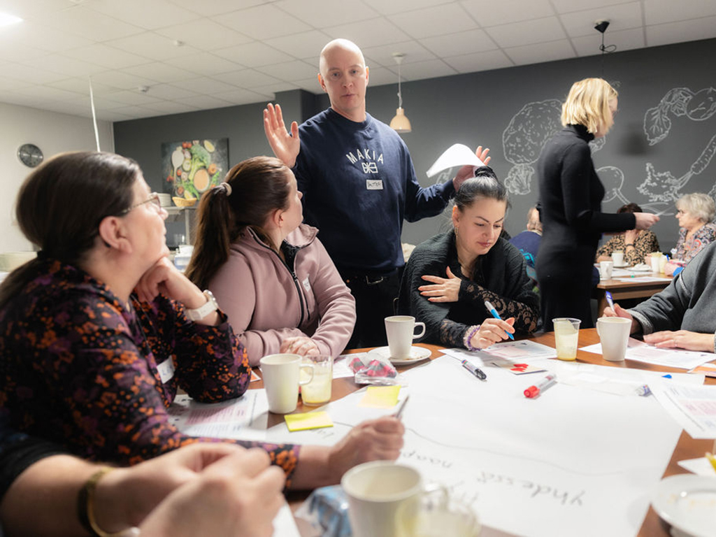 Mies ohjaa pöydän ääressä istuvia työpajalaisia.