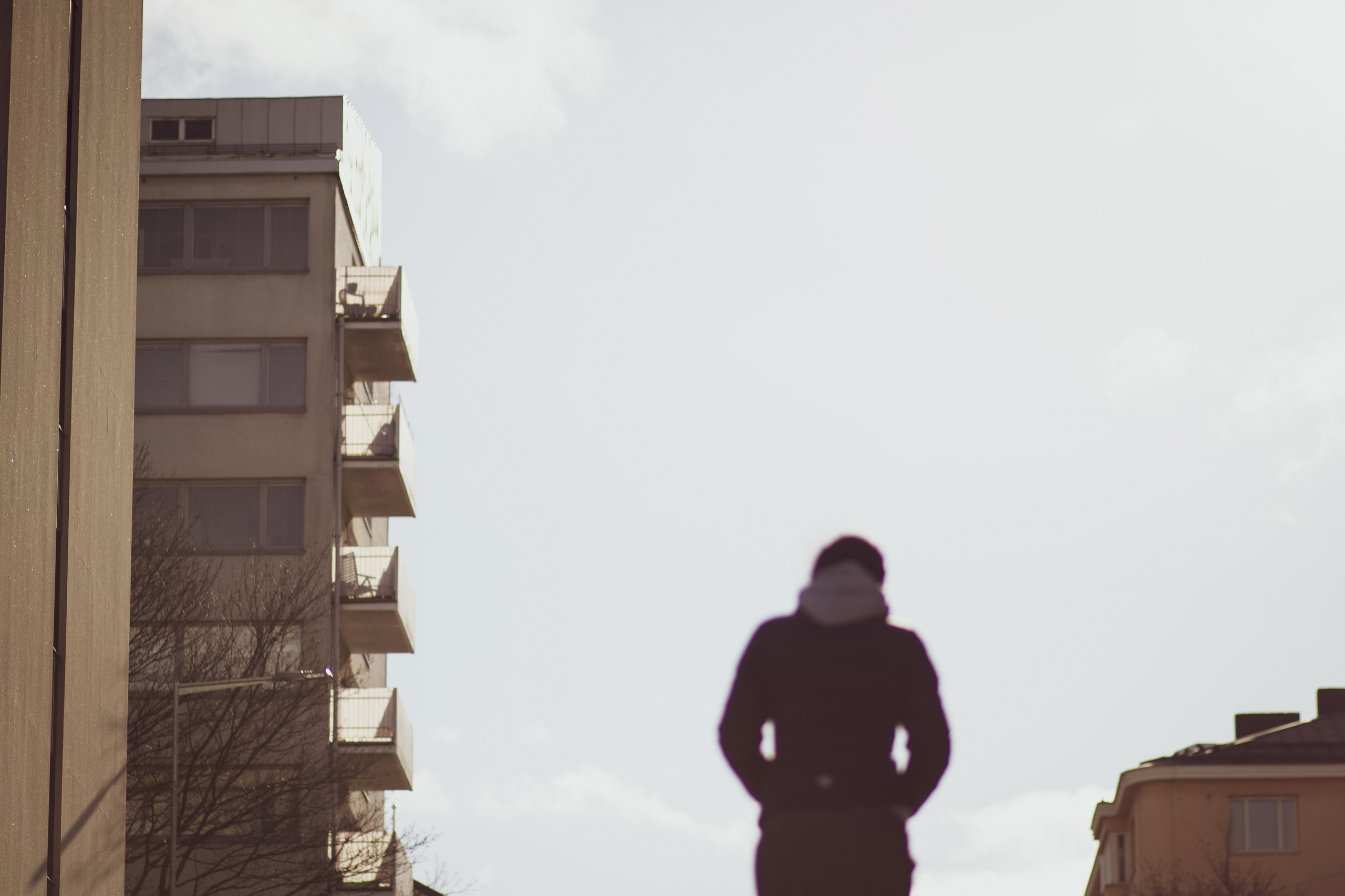 Henkilö kävelee talojen ympäröimällä kadulla kirkkaassa päivänvalossa selin kameraan.