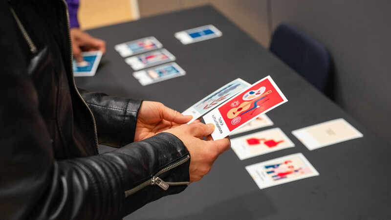 Henkilö pitelee kädessään värikkäitä kortteja pöydän ääressä, jossa on enemmän kortteja levitettynä.