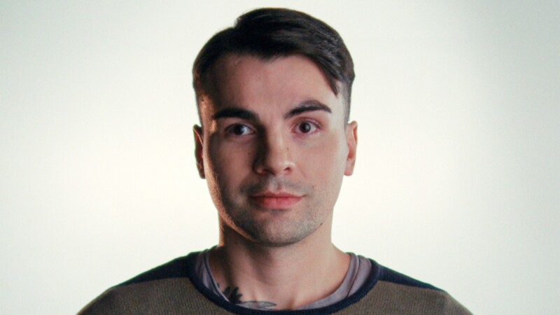 Nuori mies, lyhyet tummat hiukset, neutraali ilme vaaleaa taustaa vasten.