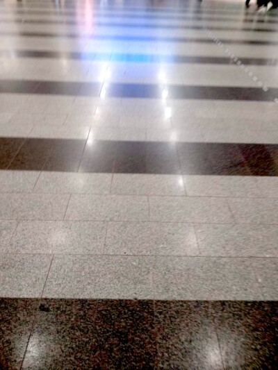 Kuvassa näkyy sisätilan lattia, jossa on laatoitettu kuviolattia vaalean harmailla ja tummanruskeilla suorakaiteen muotoisilla laatoilla.