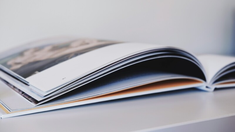 Avoin raporttikirja, jossa näkyy osittain kuvia ja tekstiä, asetettuna valkoiselle pöydälle.