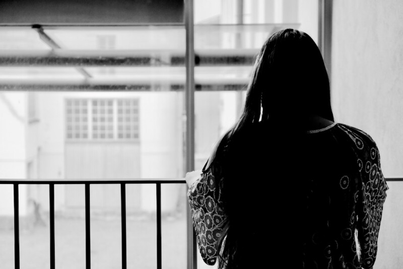 En kvinna med långt hår står med ryggen mot kameran och håller sig fast i räcket.