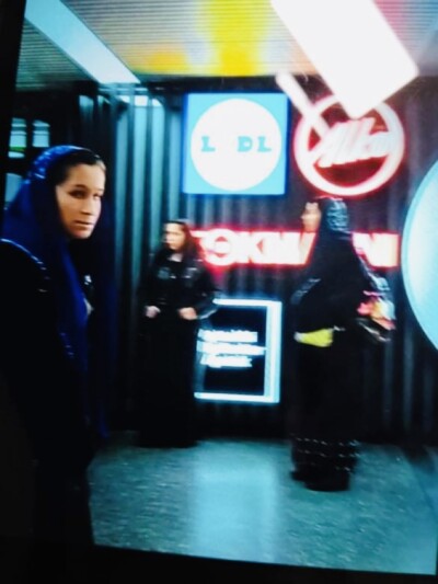 Kuvassa on kolme naista hämärässä sisätilassa, taustalla näkyy neonvaloja.