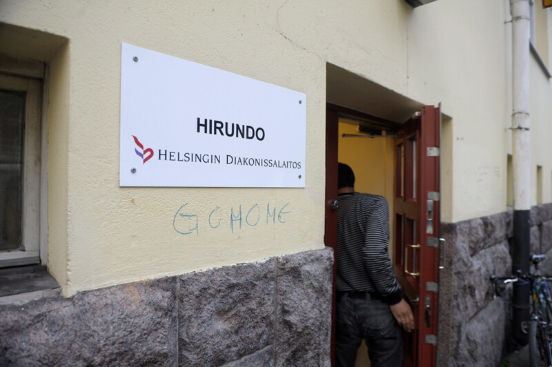 Hirundo-päiväkeskuksen seinässä kyltti Helsingin diakonissalaitos ja seinään kirjoitettu vihakirjoitus "GO HOME", mies kävelee sisäänkäynnistä.