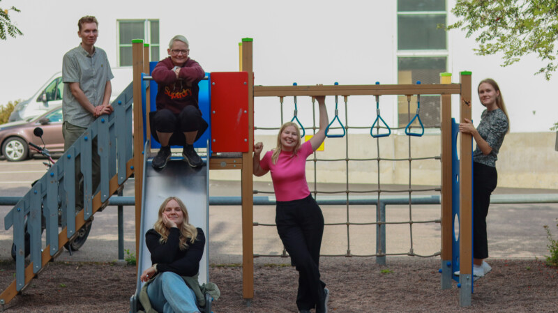 Viisi nuorta aikuista poseeraa leikkipuiston kiipeilytelineellä hymyillen; ryhmäkuva HIMA-hankkeen tiimistä, joka tukee nuorten arkea ja elämänhallintaa.