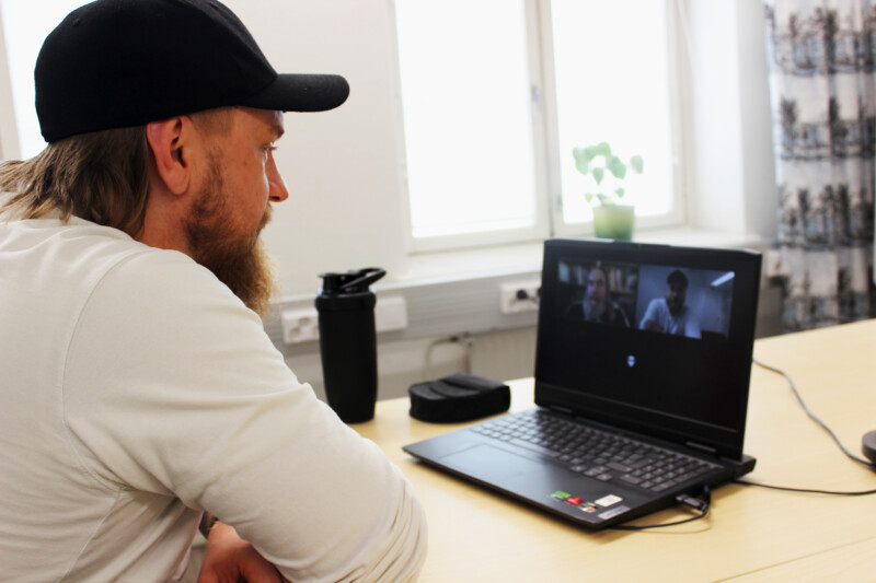 Henkilö istuu kannettavan tietokoneen ääressä, tietokoneen ruudulla näkyy oma kuva, kollegan kuva ja osallistujan kuvake.